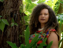 Silviane Ramos Lopes da Silva. Cenário arborizado. Mulher negra com cabelos crespos soltos. Ela veste roupa estampada.